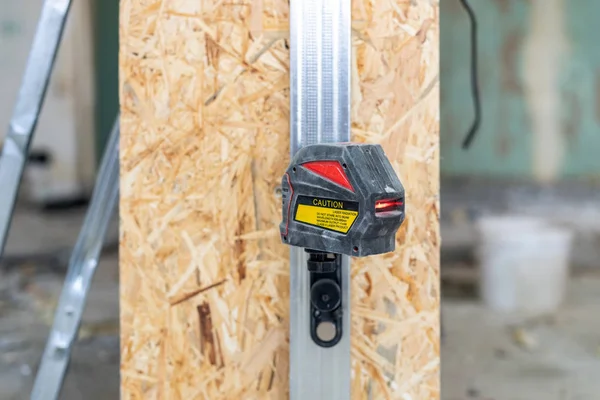 Close up photo of laser level with a red beam stand against room with oriented strand board panel