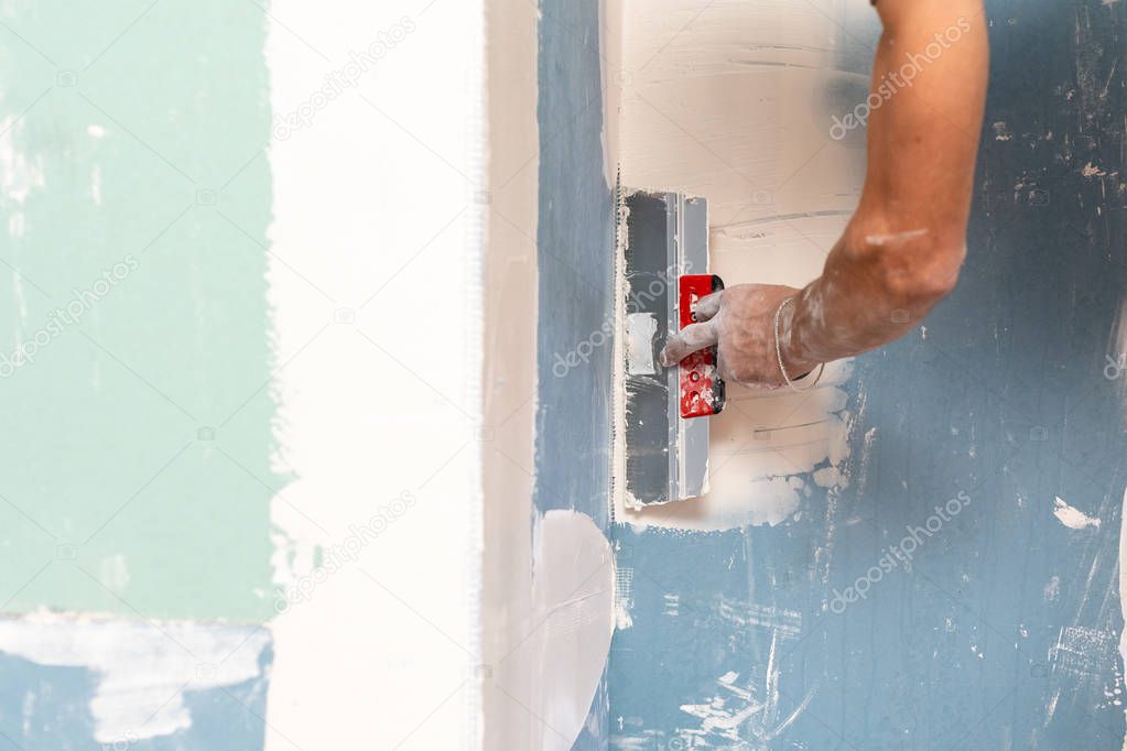 Cropped close up photo of professional repairman hand with spatula plastering and remodel wall inside room with gypsum element making renovation interior