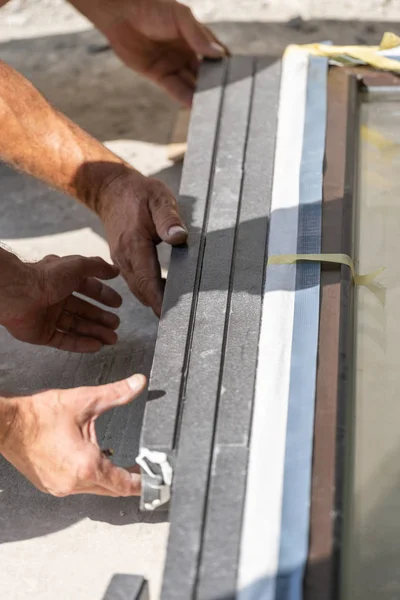 Vertical photo of two mature handyman holding together two elements of plastic window frame and assembly construction together