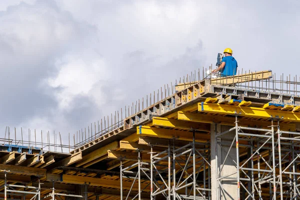 Low angle top and rear back behind view photo of  professional collar occupation in protect safe helmet standing on unfinished multistory. He looking at special device on iron support elements