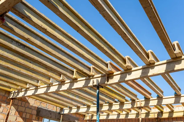 Low angle top view photo of formwork construction. Small unfinished building with wooden ceiling beam on support pipes under blue sky
