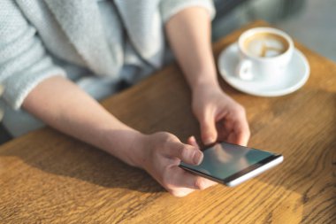 Üstten görünüm ve taşınabilir telefon donanımları elinde bayanla kırpılmış fotoğrafı yukarıda yüksek açı. O masada içecek bir fincan ile oturan loft Restaurant'ta iç mekan içinde
