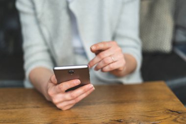 Taşınabilir telefon donanımları elinde bayanla kırpılmış fotoğrafı kapatın. Ekranda loft restoran ve işaretçi işaret parmağı içinde iç mekan içinde oturan