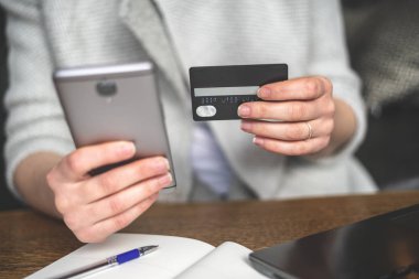 Taşınabilir telefon donanımları ve elinde plastik kart tanınmaz bayanla kırpılmış fotoğrafı kapatın. O restoranda çatı iç mekan içinde oturuyor ve çevrimiçi alışveriş yapma