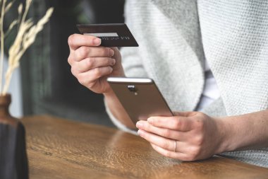 Bayan loft Restaurant'ta iç mekan içinde kırpılmış fotoğrafı yan görünümü kapatın. O koltukta oturuyor ve taşınabilir telefon donanımları, elinde tutan kartı kullanarak