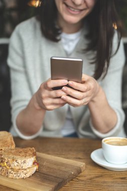 Dikey çekici tanınmaz Bayan taşınabilir telefon donanımları elinde tutan ve gülümseyen fotoğrafını kırpılmış. Loft Restaurant'ta iç mekan içinde oturan