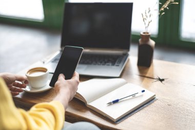 Bayan kişinin fotoğrafını yiyecek, İçecek, taşınabilir telefon donanımları el loft Restaurant'ta iç mekan içinde oturan bir fincan ile kesilmiş. Not defteri ve dizüstü bilgisayar arka plan bulanık ile seçici odak