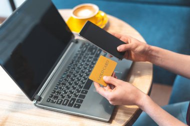 Genç bayan kafede oturuyor ve modern cep telefonu, dizüstü bilgisayarını kullanıyor.