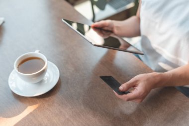 Genç bayan kafede oturuyor ve kredi kullanarak tablet bilgisayar kullanıyor.