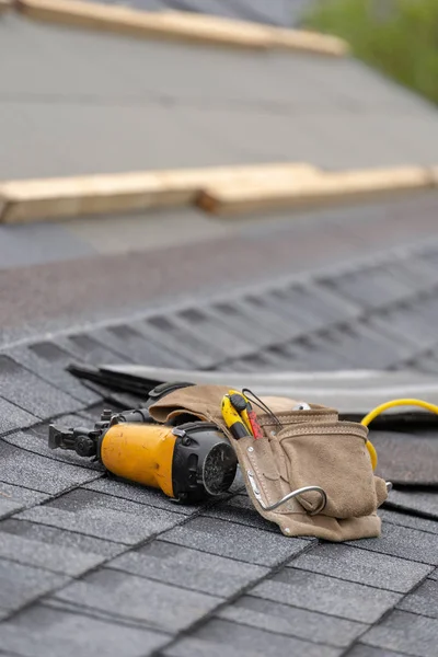 Techo de baldosas de asfalto y cinturón de herramientas acostado en la nueva casa bajo constru — Foto de Stock