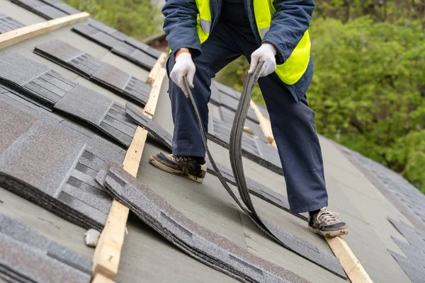 Працівник встановлює плитку на дах нового будинку під час будівництва — стокове фото
