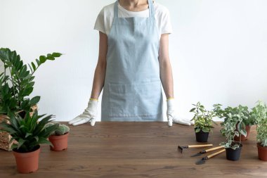 Bir kadın saksıda çiçeklerle masanın yanında duruyor.