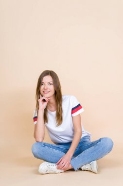 Young woman with crossed legs sitting on pastel beige background