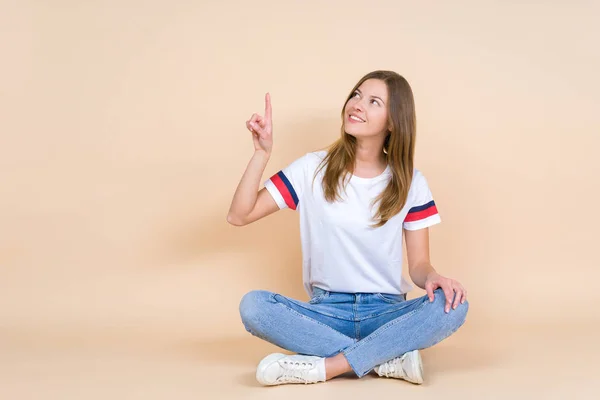 Young woman with crossed legs sitting on pastel beige background