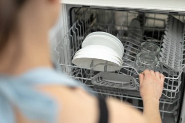 Tabak ve bardakile modern bulaşık makinesi ni açan kadın, mutfakta duruyor 