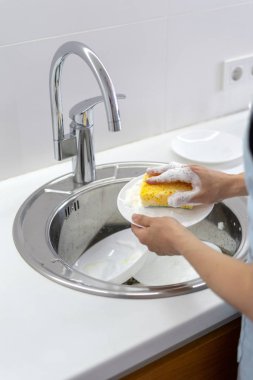 Köpük ile sünger kullanan kadın, beyaz mutfakta lavaboda plaka yıkama