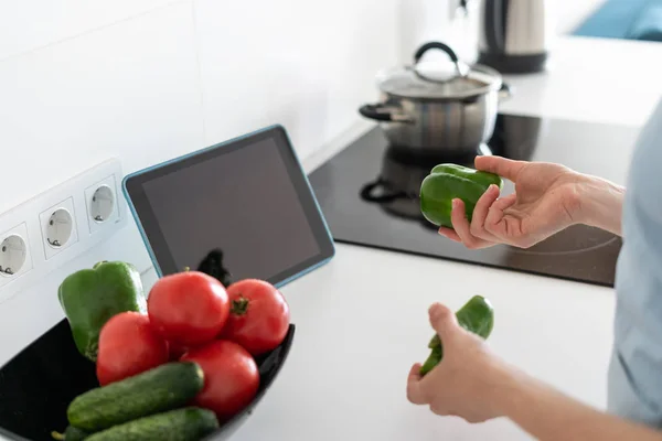 Женщина готовит еду на кухне с цифровой планшет на столе, держа в руках овощи — стоковое фото