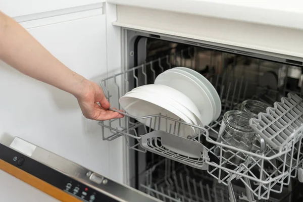 Женщина открывает современную посудомоечную машину с тарелками и чашками, стоя на кухне — стоковое фото