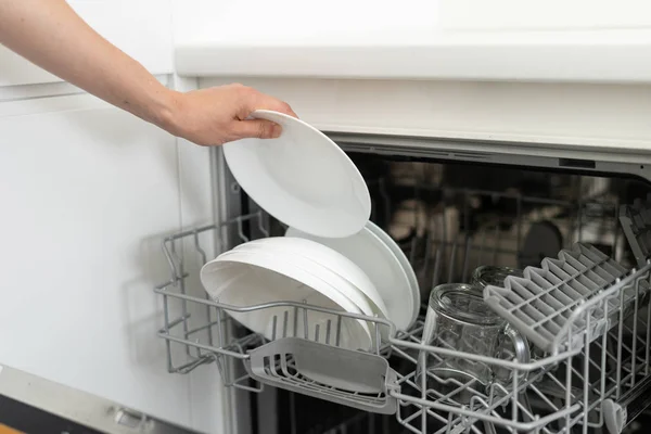 Женщина стоит рядом с современной посудомоечной машиной с тарелкой в руке — стоковое фото