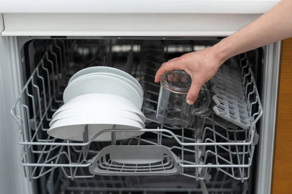 Открытая современная посудомоечная машина с тарелками, держащими в руке чистую чашку — стоковое фото