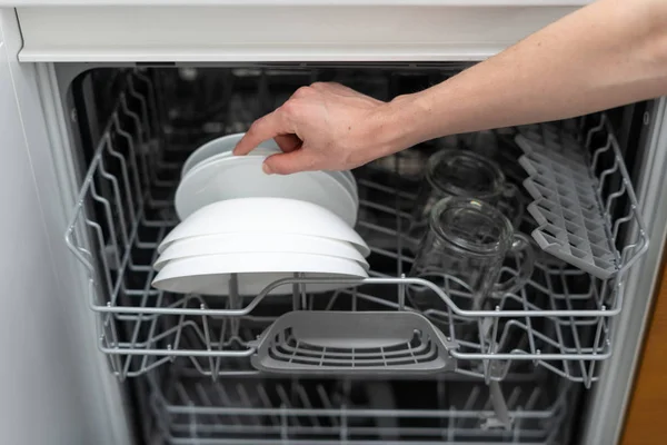 Woman standing near modern dishwasher machine with plate in hand — Stock Photo, Image