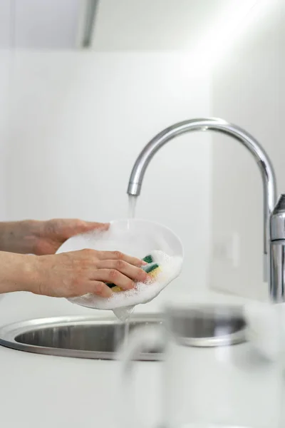 Mujer usando esponja con espuma, placa de lavado en fregadero en la cocina blanca — Foto de Stock