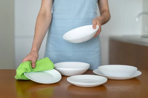 Woman cleaning plates and bowls on kitchen with wooden table