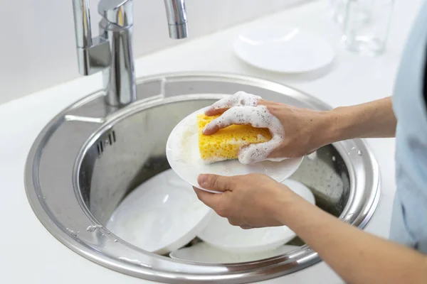 Mujer usando esponja con espuma, placa de lavado en fregadero en la cocina blanca — Foto de Stock