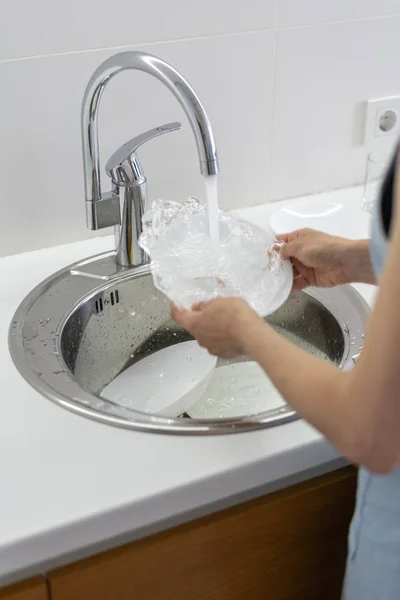 Woman washing plate in sink at white kitchen