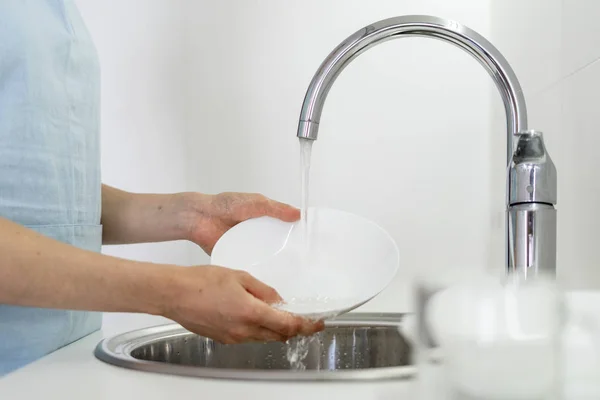 Женщина моет посуду в раковине на белой кухне — стоковое фото