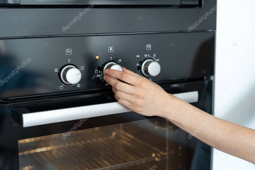 Woman select program turning switch at modern built in oven