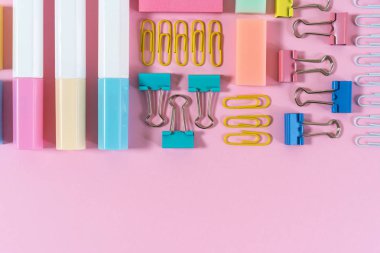 Pembe pastel arka plan üzerine kırtasiye, marker ve ataş