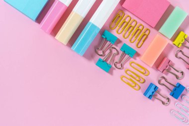 Pembe pastel arka plan üzerine kırtasiye, marker ve ataş