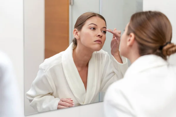 Mujer en albornoz mirando en el espejo en el baño — Foto de Stock