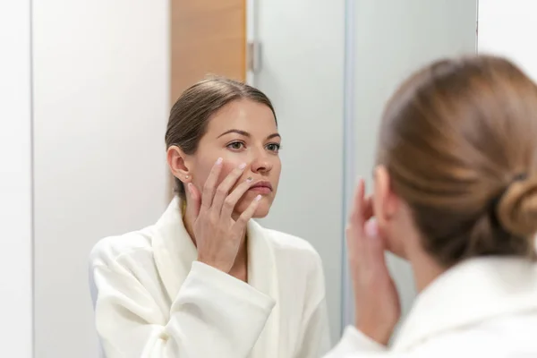 Mujer en albornoz mirando en el espejo en el baño — Foto de Stock