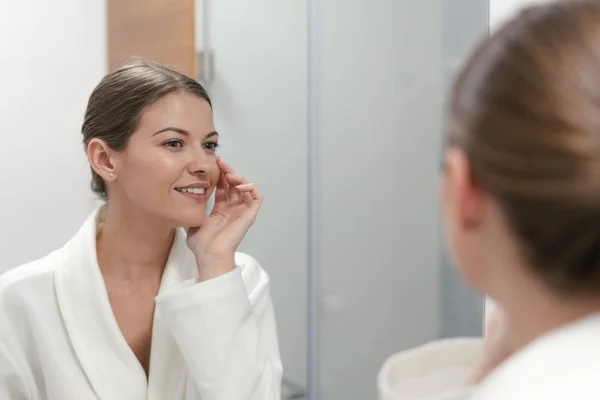 Femme en peignoir regardant dans le miroir à la salle de bain — Photo