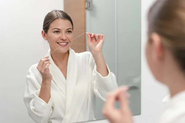 Woman in white bathrobe holding dental floss in hands — Stock Photo, Image