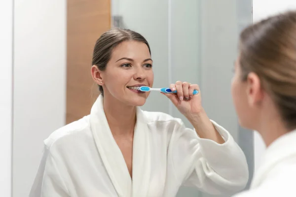 Donna in accappatoio bianco in possesso di spazzolino da denti, in piedi in bagno — Foto Stock