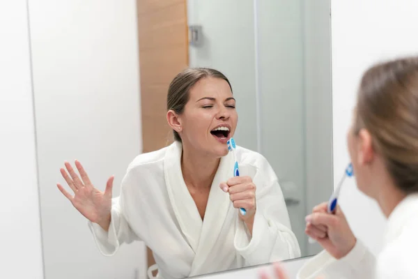 Wanita bermantel putih memegang sikat gigi, berdiri di kamar mandi — Stok Foto