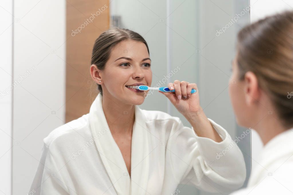 Woman in white bathrobe holding toothbrush, standing in bathroom