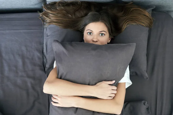 Jong volwassen vrouw liggend op bed en knuffelen kussen — Stockfoto