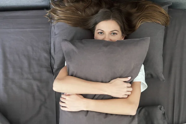 Jong volwassen vrouw liggend op bed en knuffelen kussen — Stockfoto