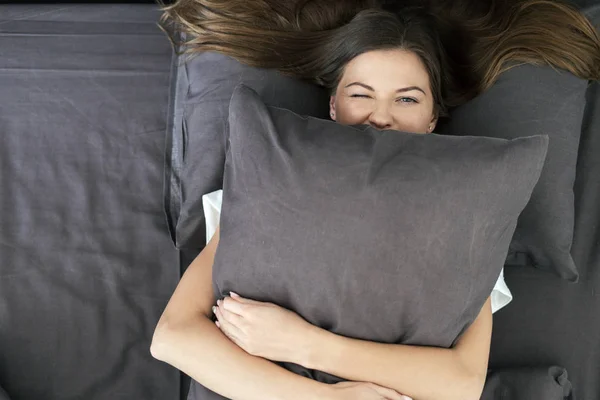 Junge erwachsene Frau liegt auf Bett und umarmt Kissen — Stockfoto