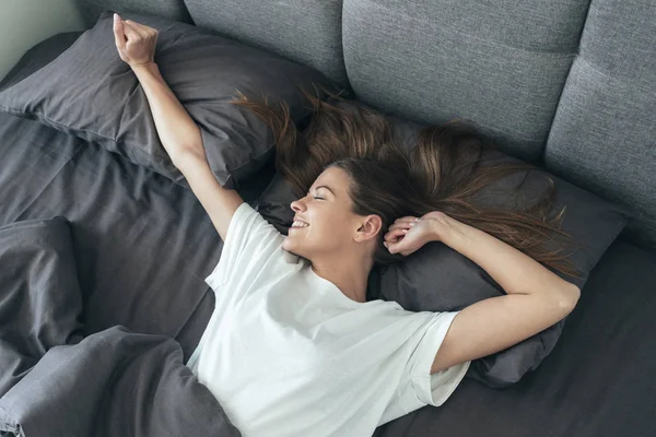 Jong volwassen vrouw awaiking op bed in de ochtend — Stockfoto