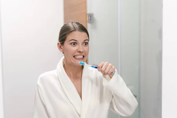 Wanita bermantel putih memegang sikat gigi, berdiri di kamar mandi — Stok Foto