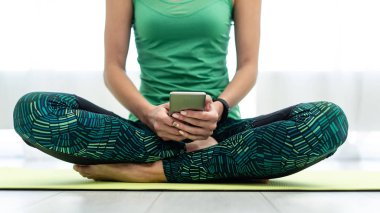 Akıllı telefon kullanan genç sportif kadın, fitness mat üzerinde oturan 