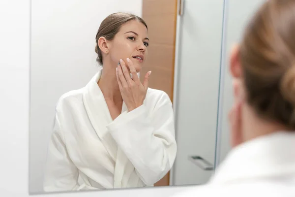 Mujer en albornoz mirando en el espejo en el baño — Foto de Stock