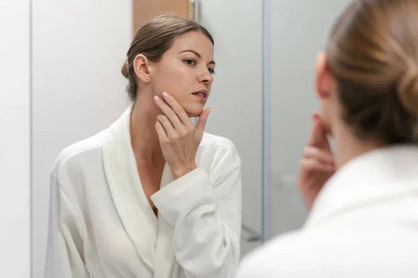 Mujer en albornoz mirando en el espejo en el baño — Foto de Stock