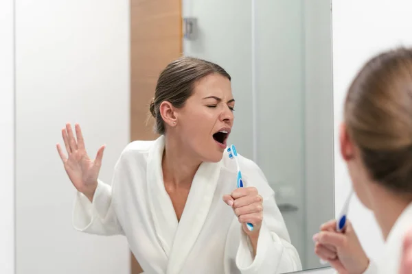 Žena v bílém županu drží zubní kartáček, stojící v koupelně — Stock fotografie