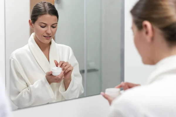 Woman holding cream in hands, standing at bathroom — Stock Photo, Image